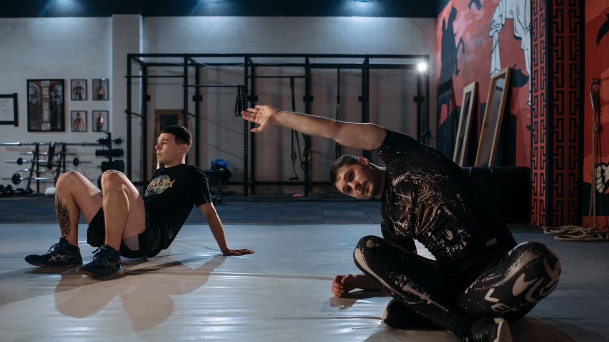 Two men stretching on the gym floor, preparing for a workout session.